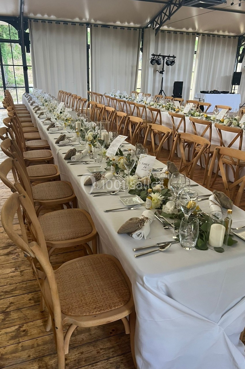 Grande table de réception décorée avec élégance, nappes blanches, vaisselle raffinée et chaises en bois dans une salle…