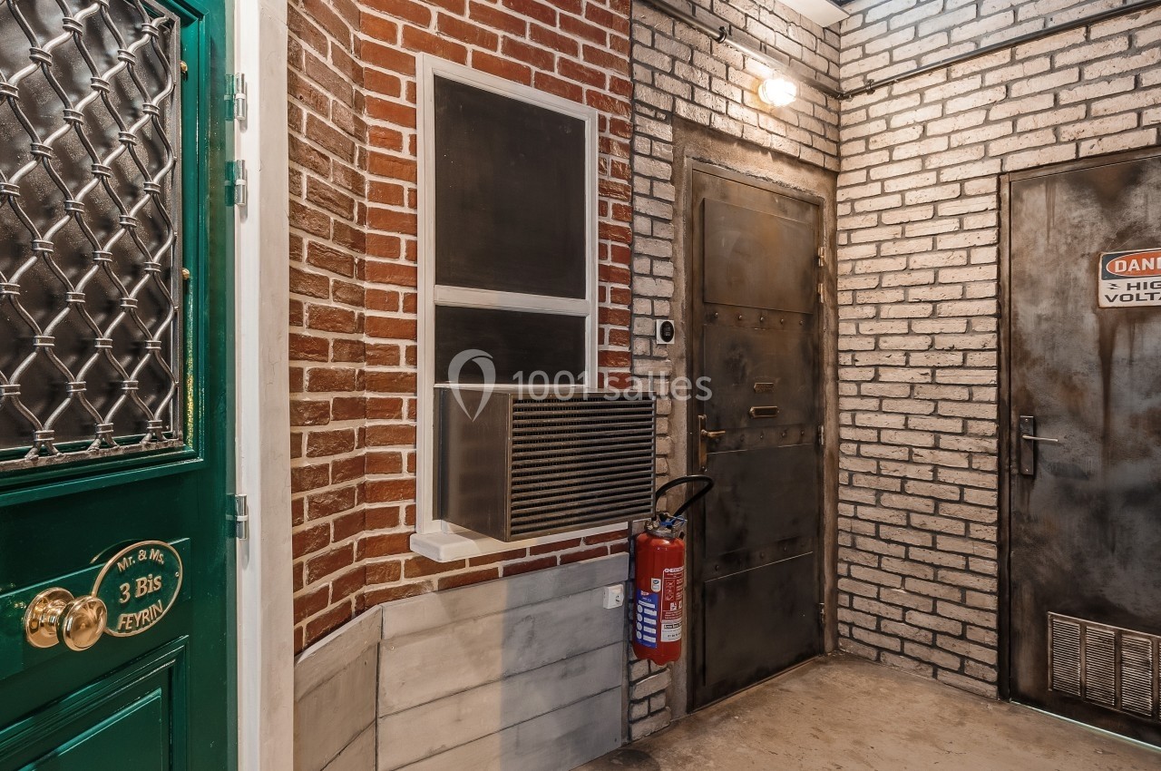 Entrée d'un bâtiment avec murs en briques, porte verte, porte métallique et extincteur fixé au mur.