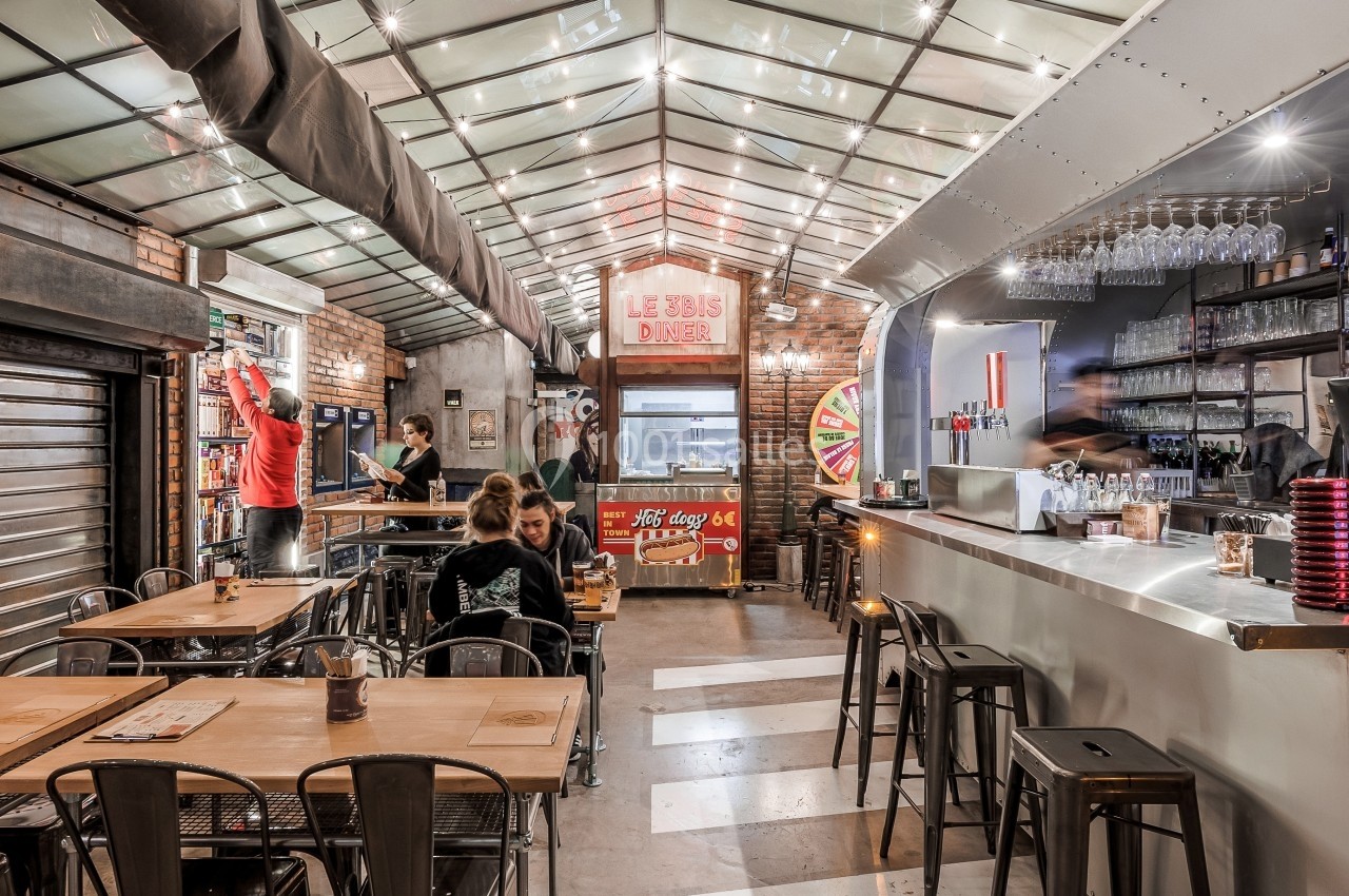 Intérieur d'un restaurant avec tables en bois, bar moderne, éclairage suspendu et ambiance conviviale.