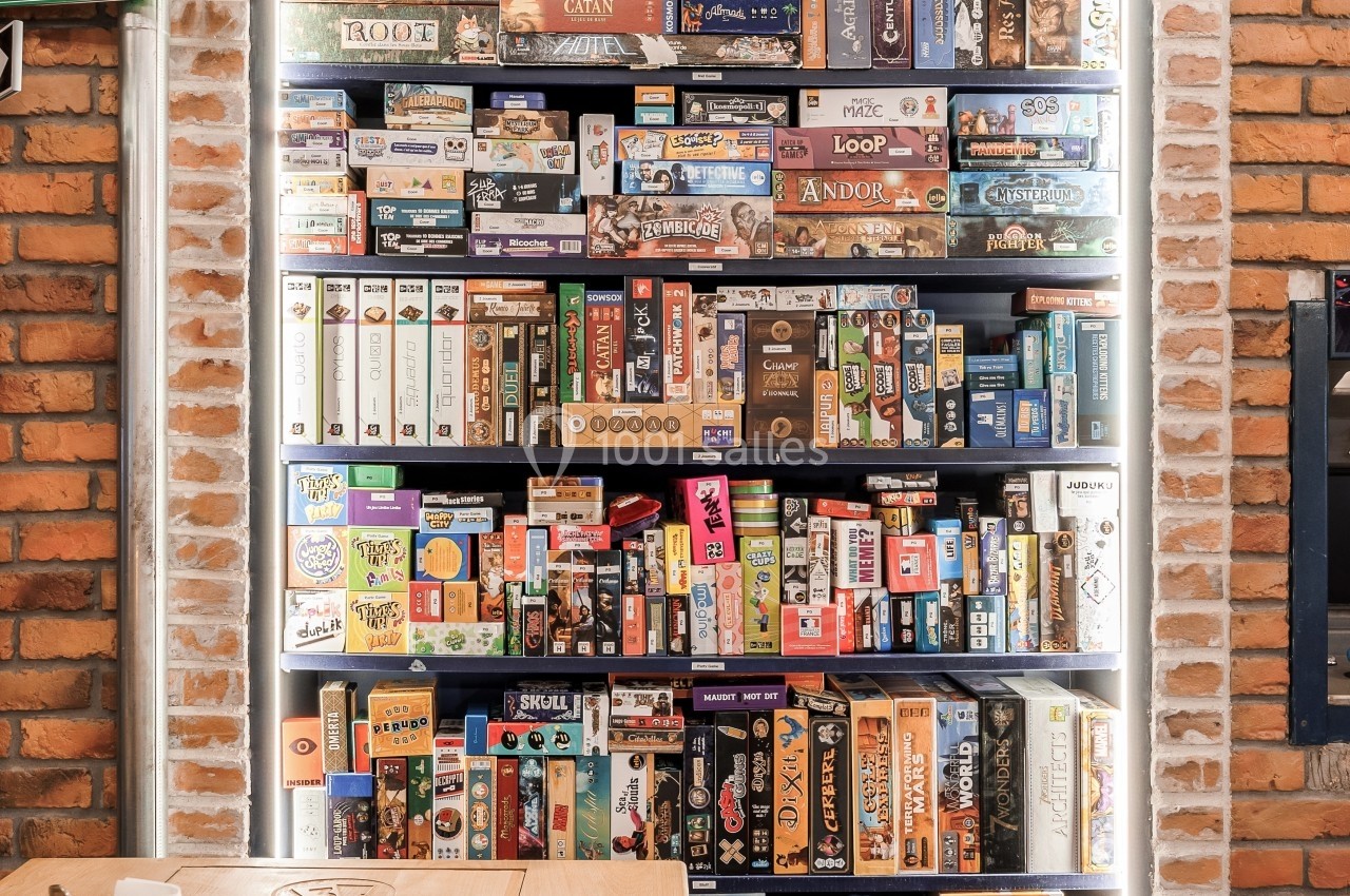 Étagère remplie de jeux de société variés dans un espace intérieur avec murs en briques.
