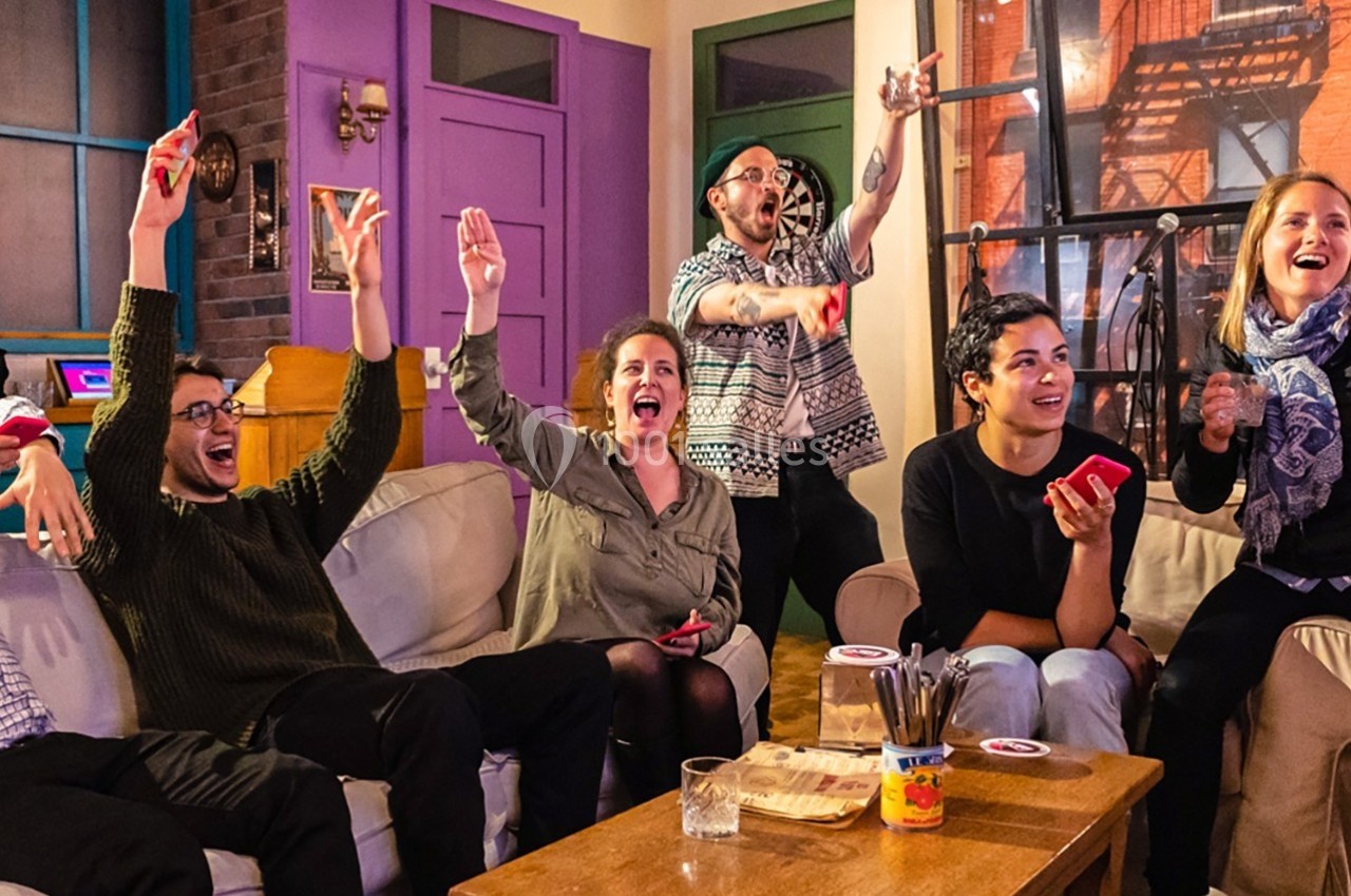 Des personnes assises dans un salon, souriantes et levant les bras, semblant célébrer ou jouer ensemble.