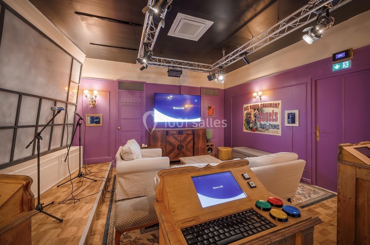 Salle équipée de canapés, écrans, micros et buzzers, décorée dans des tons violets avec des éléments rétro.