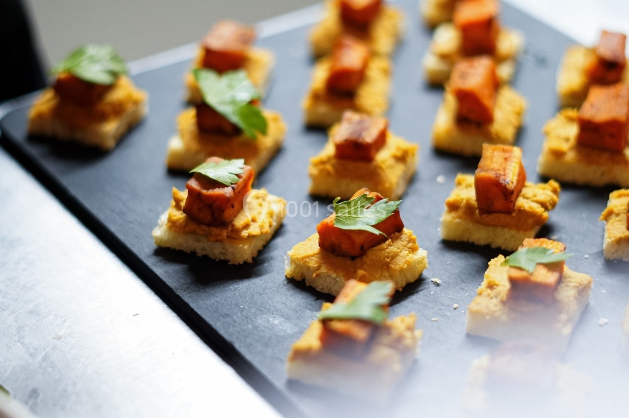 Bouchées apéritives sur une ardoise, composées de pain, de patate douce rôtie et décorées de feuilles de persil.