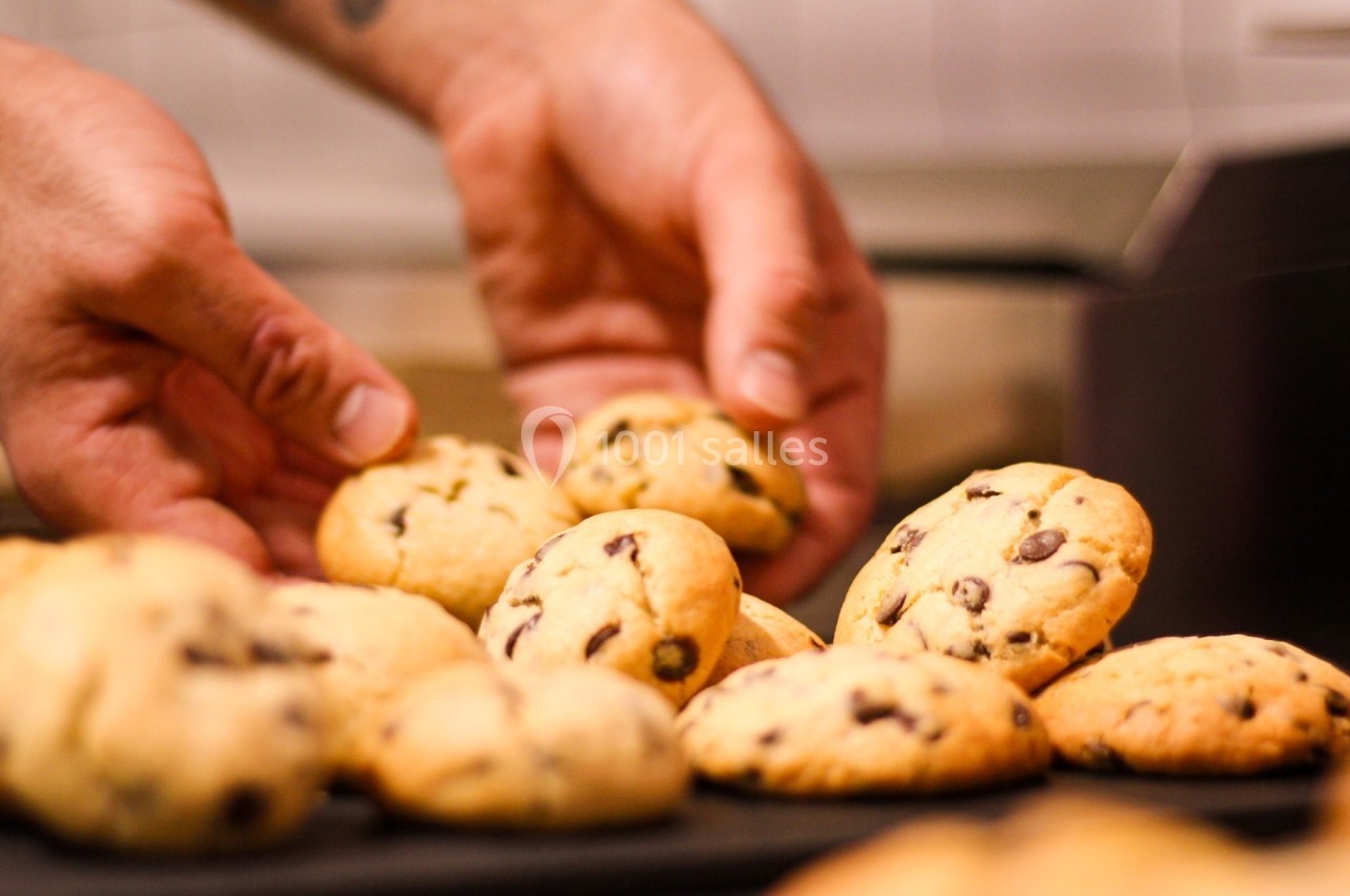 Mains disposant des cookies aux pépites de chocolat sur un plateau dans une cuisine.
