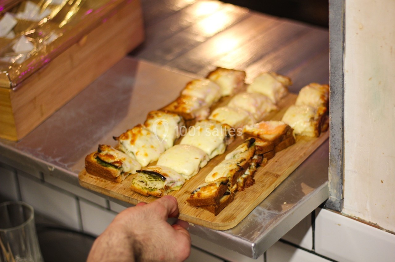 Tranches de pain garnies de fromage fondu et autres ingrédients, servies sur une planche en bois.