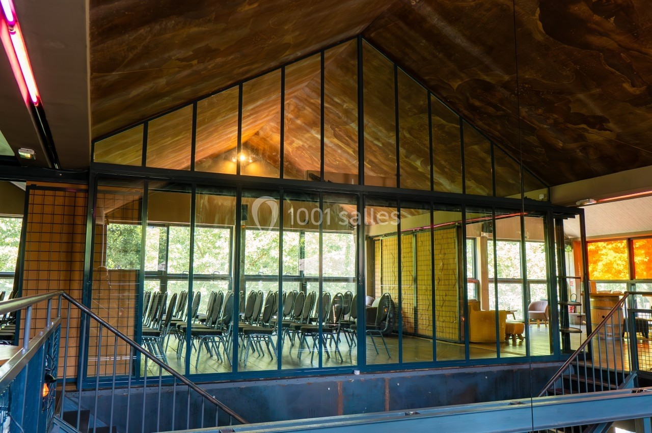 Salle de réunion vitrée avec des chaises alignées, entourée de murs en briques et vue sur l'extérieur verdoyant.