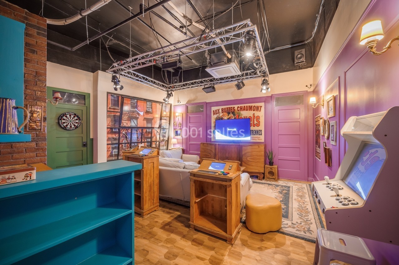 Salle de jeux rétro avec canapé, bornes d’arcade, cible de fléchettes et décorations murales colorées.