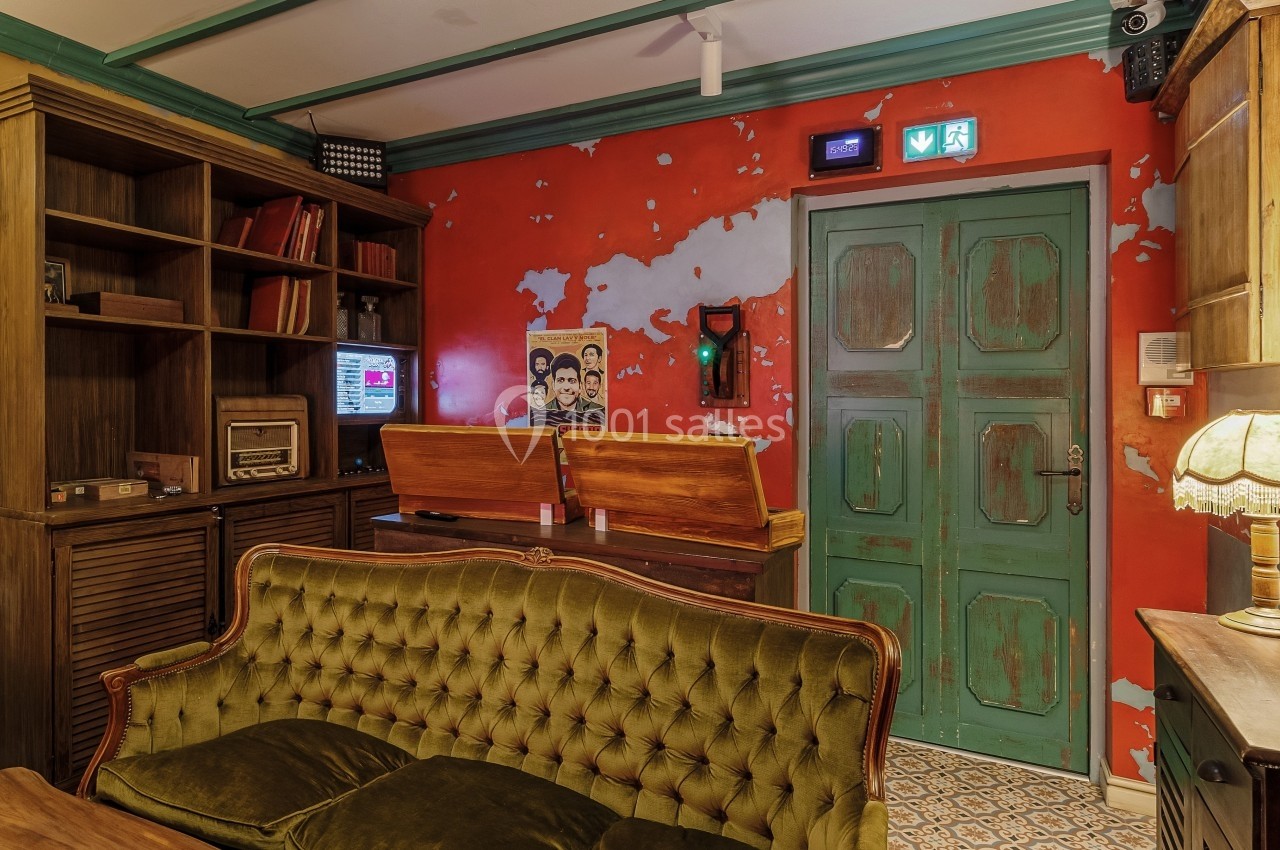 Salon rétro avec canapé en velours vert, bibliothèque en bois, murs rouges usés et porte verte vintage.