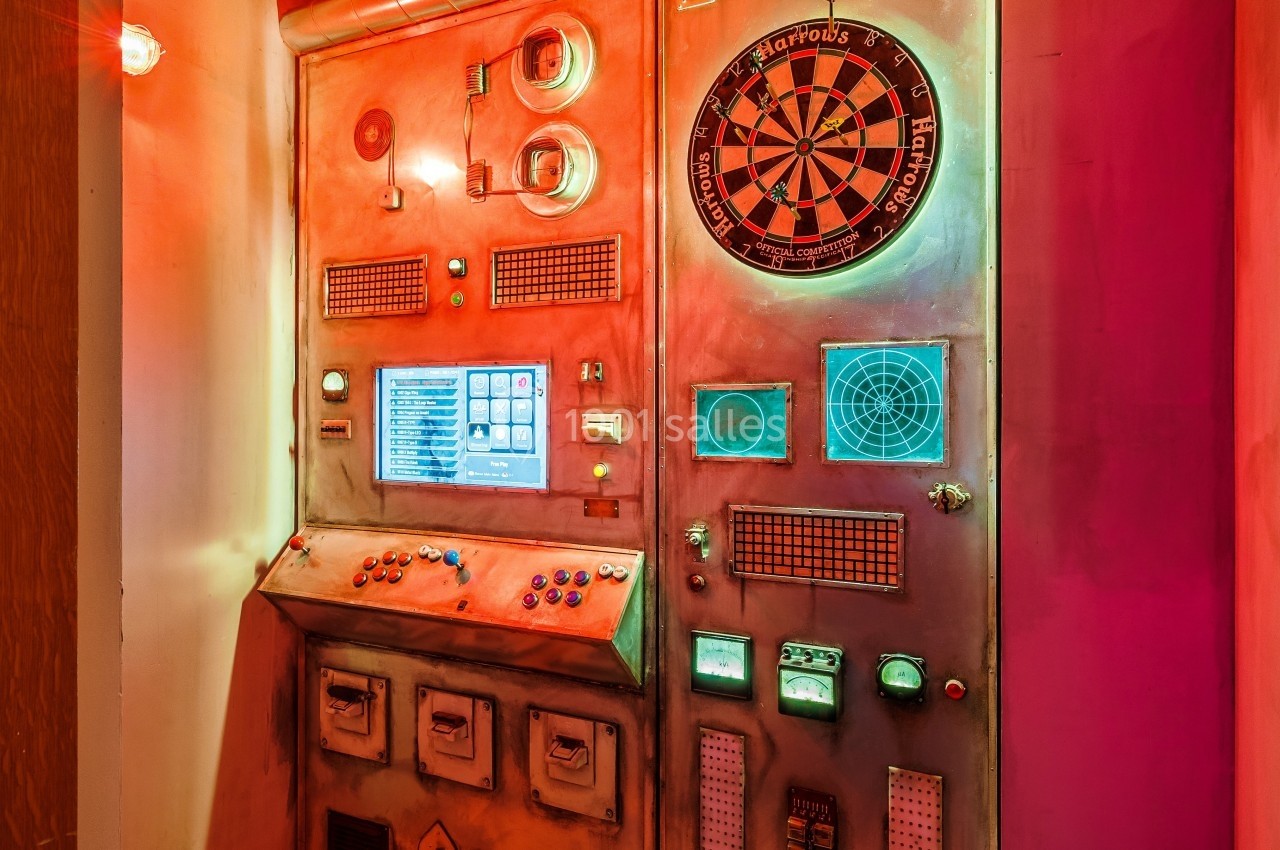 Panneau de commande rétro-futuriste avec cadrans, écrans, boutons et une cible de fléchettes intégrée.