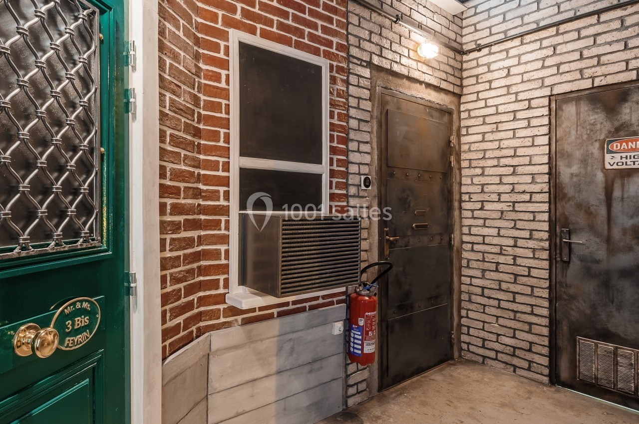 Entrée d'un bâtiment avec murs en briques, porte verte, porte métallique et extincteur fixé au mur.