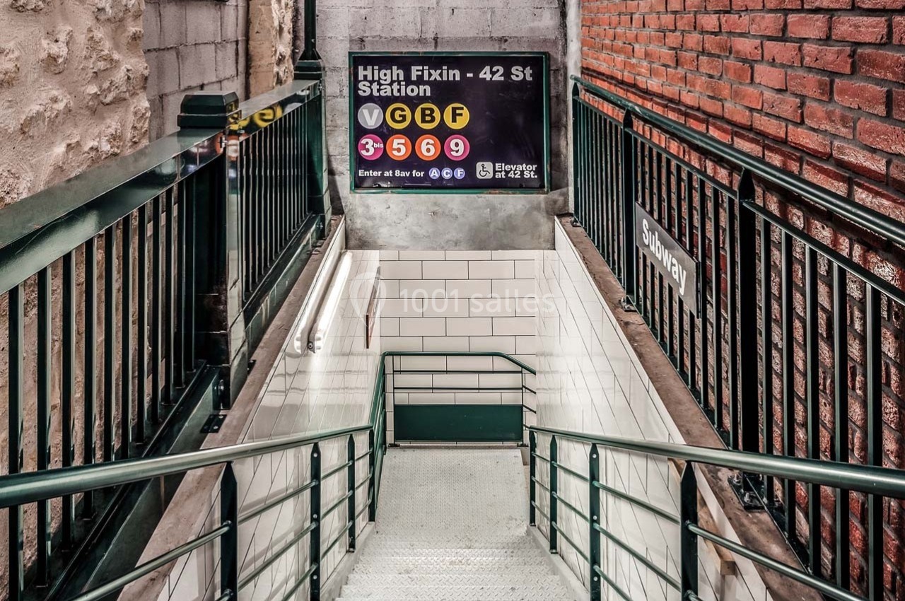 Escalier descendant vers une station de métro, entouré de murs en briques et panneaux indiquant les lignes disponibles.