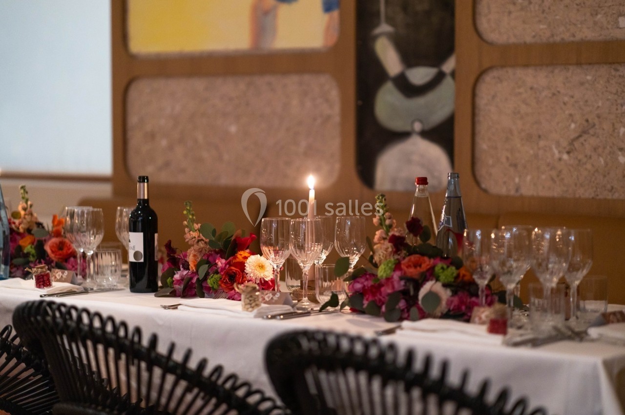Table élégamment dressée avec nappes blanches, verres, bougie allumée, fleurs colorées et bouteilles de vin et d'eau.