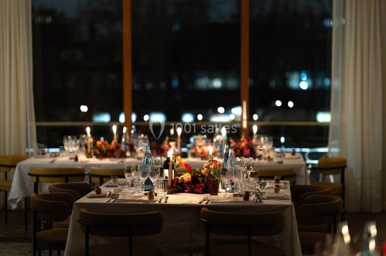 Salle de réception élégamment décorée avec des tables dressées, des bougies allumées et des fleurs colorées.