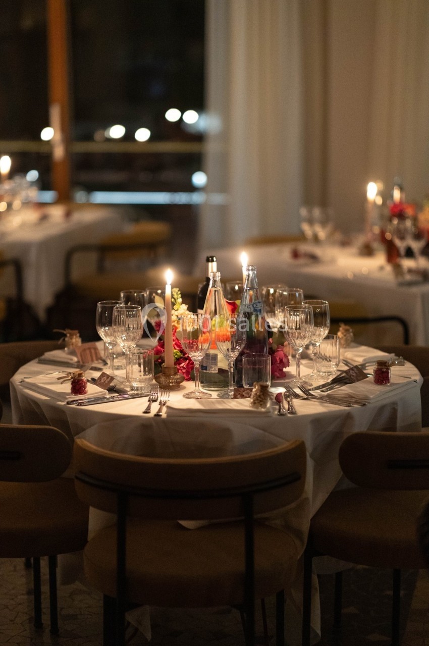 Table élégamment dressée avec nappes blanches, verres, bougies allumées et décorations florales dans une ambiance tamisée.