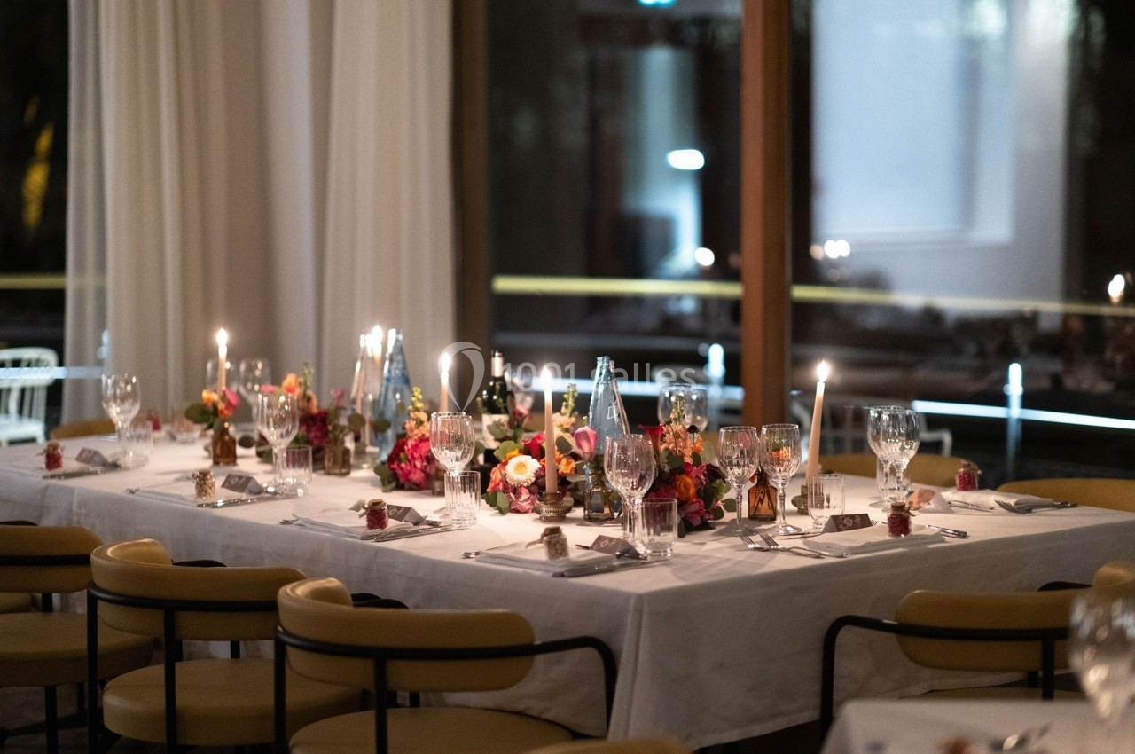 Table élégamment dressée avec nappes blanches, bougies allumées, fleurs colorées et verres en cristal dans une salle…