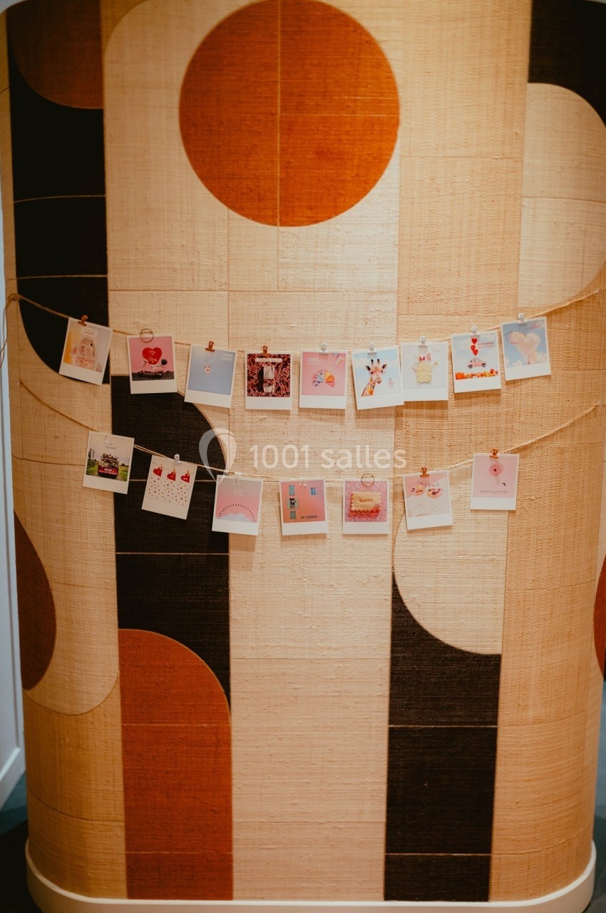 Photos suspendues sur une corde avec des pinces, accrochées devant un mur au motif géométrique beige et marron.