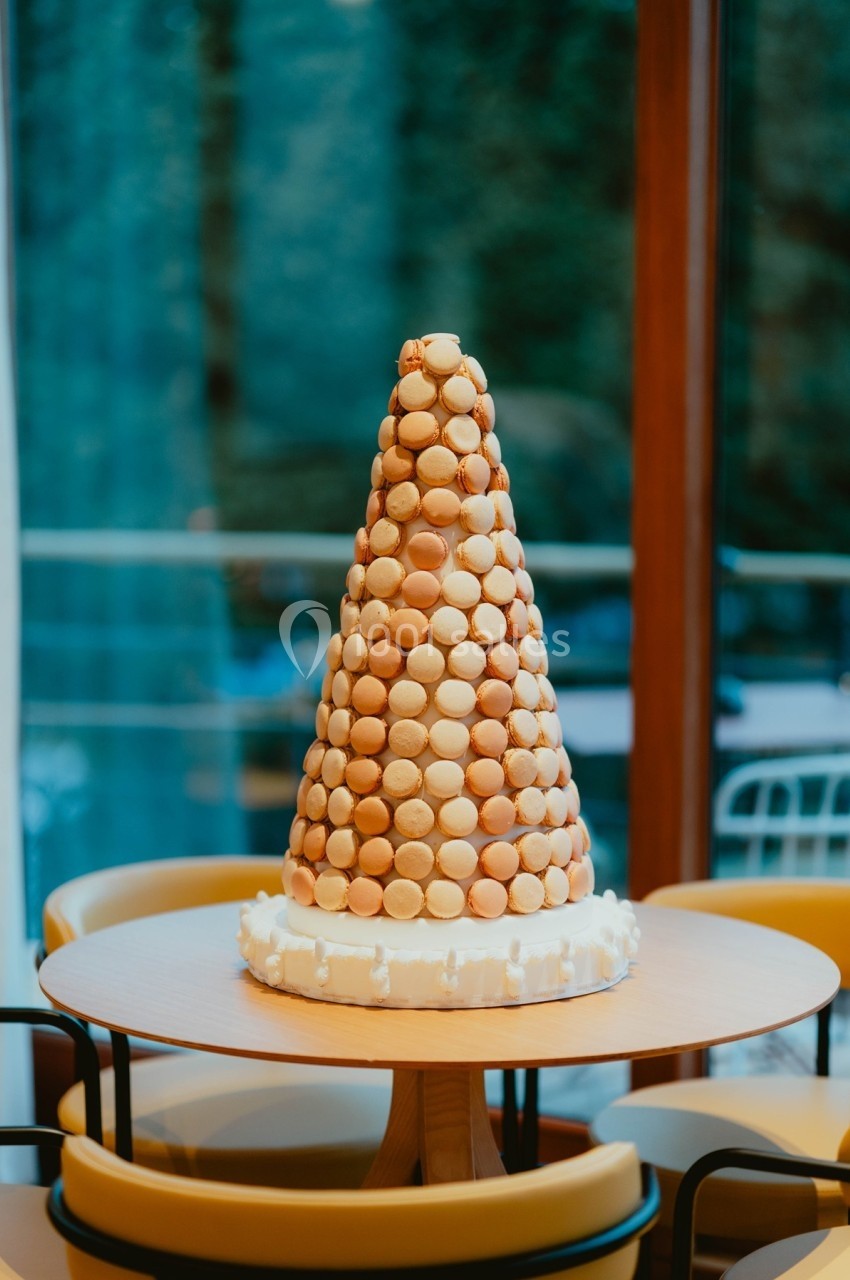 Tour de macarons beige en forme de cône, posée sur une table ronde dans un intérieur lumineux.