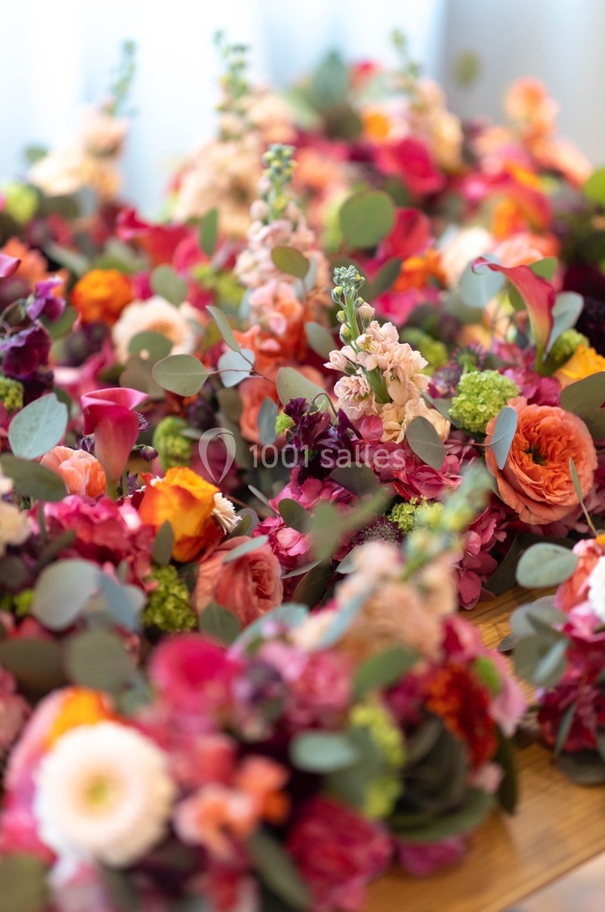 Bouquets colorés de fleurs variées avec des roses, des dahlias et des feuillages verts disposés sur une table en bois.