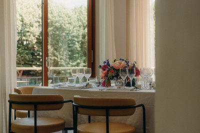 Terrasse ensoleillée avec tables rondes blanches, chaises et coussins jaunes, vue sur des toits et des arbres.