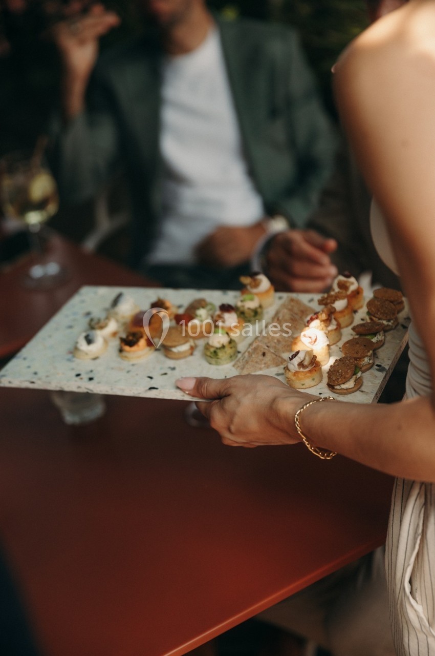 Personne tenant un plateau de petits amuse-bouches variés lors d'un événement en extérieur.