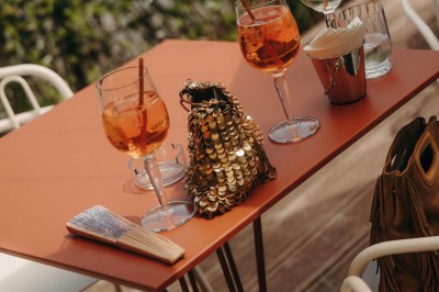 Terrasse ensoleillée avec tables rondes blanches, chaises et coussins jaunes, vue sur des toits et des arbres.