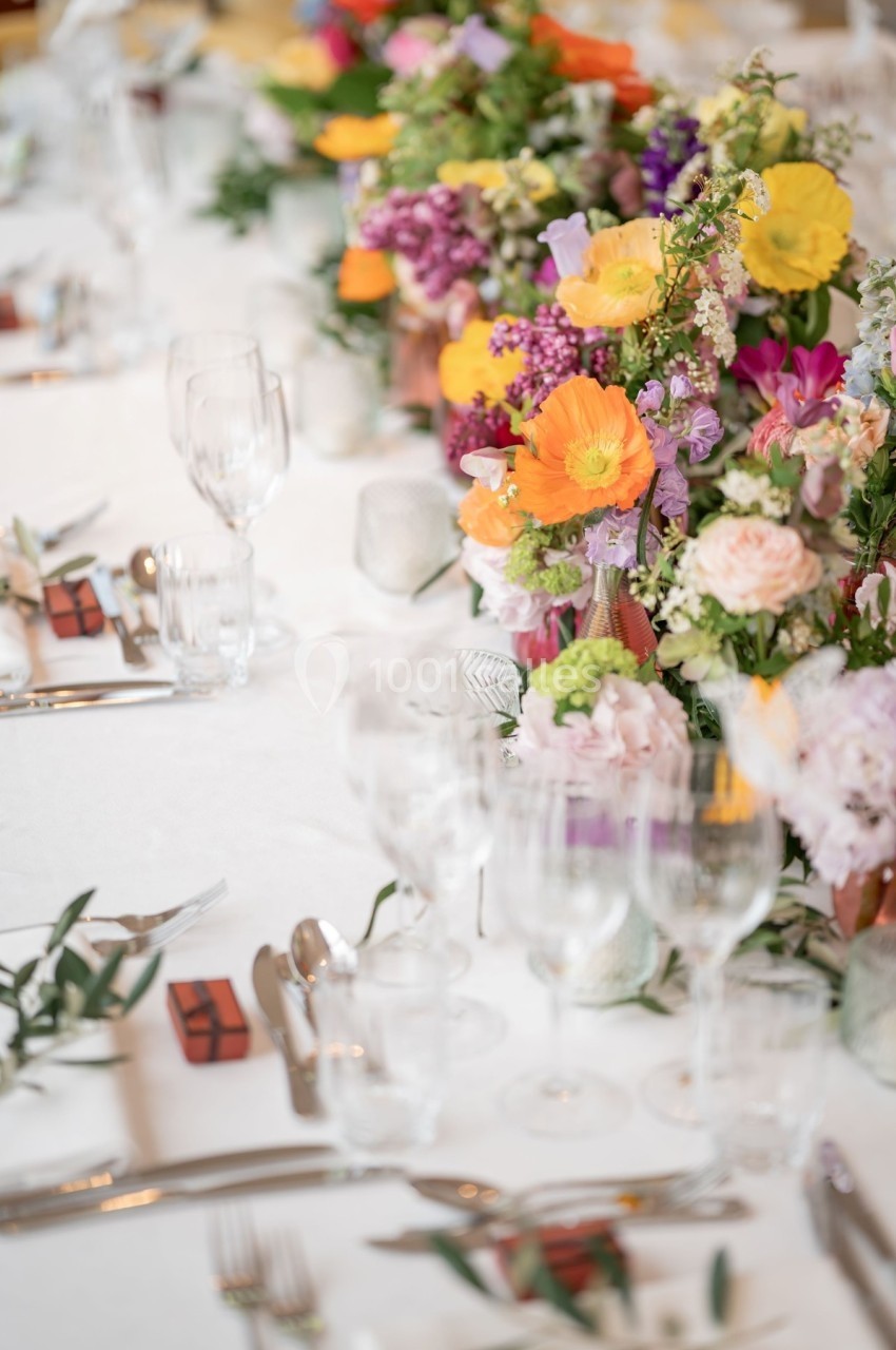 Table dressée avec des couverts, verres et centres de table composés de fleurs colorées.