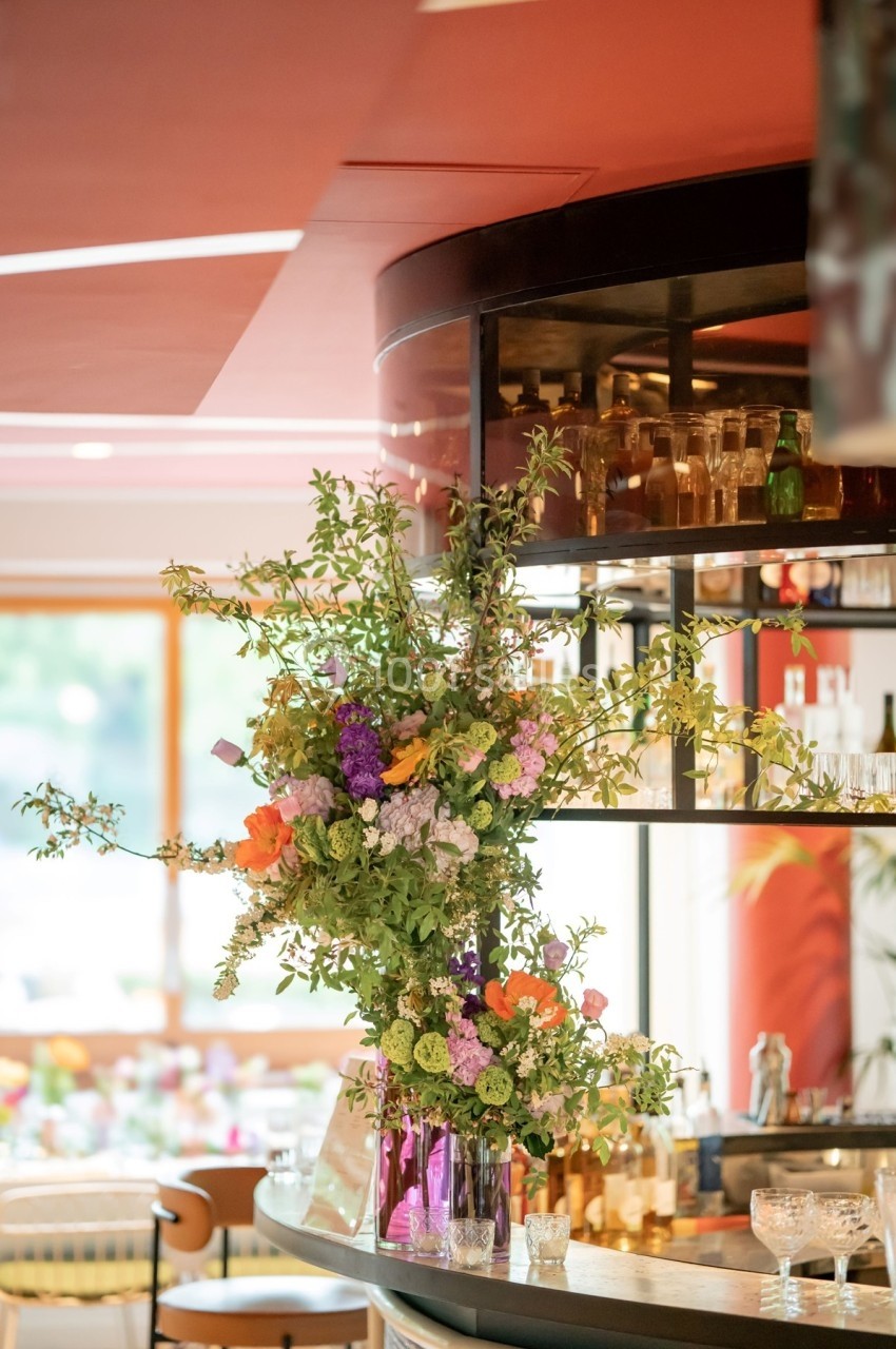 Arrangement floral coloré sur un comptoir de bar moderne avec étagères en verre et lumière naturelle en arrière-plan.