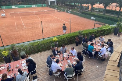 Terrasse ensoleillée avec tables rondes blanches, chaises et coussins jaunes, vue sur des toits et des arbres.