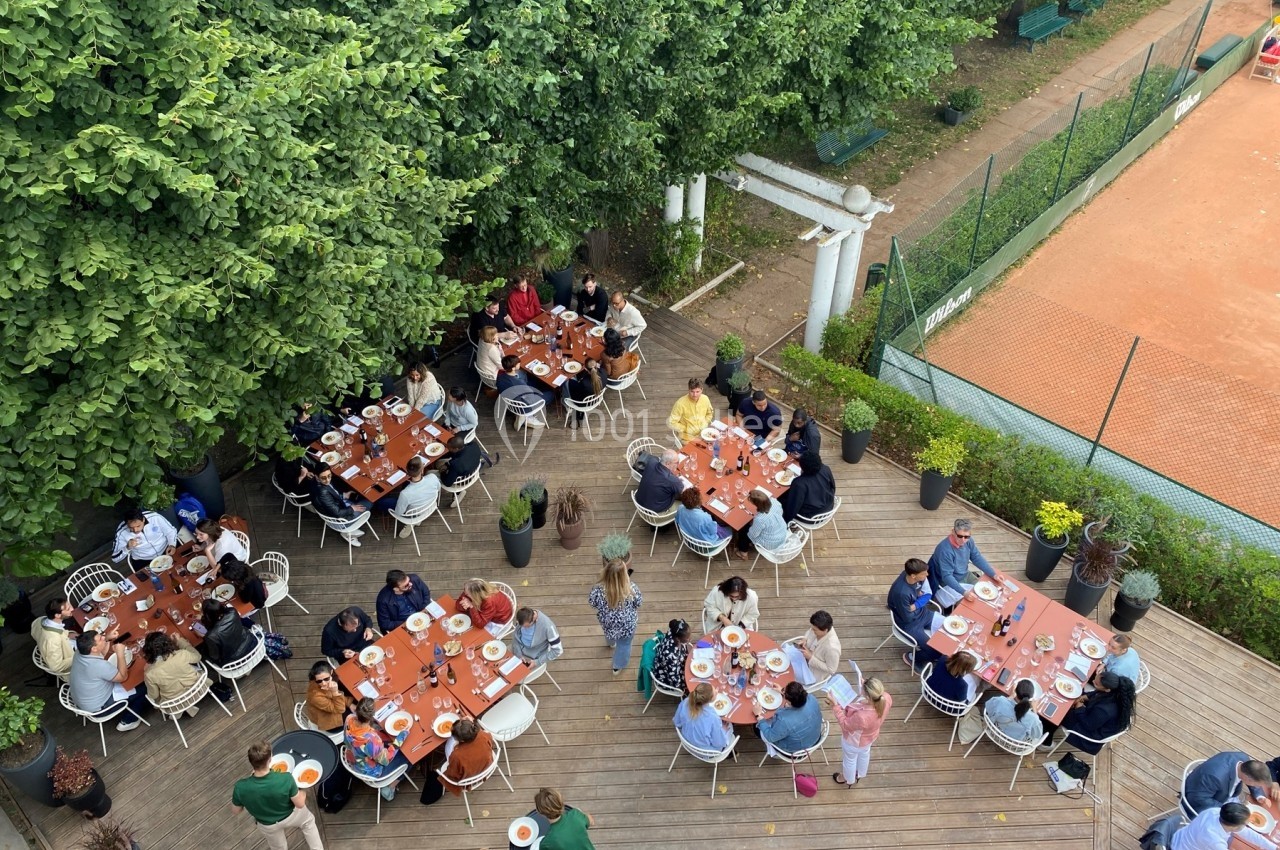 Vue aérienne d'un groupe de personnes partageant un repas en plein air sur une terrasse entourée d'arbres et d'un terrain de…