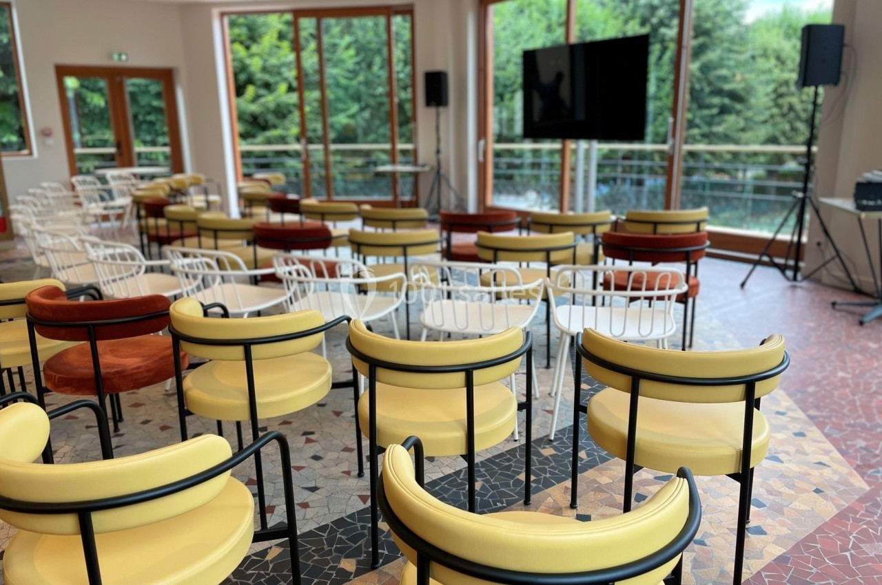 Salle de conférence lumineuse avec des chaises colorées disposées face à un écran, grandes baies vitrées donnant sur un…