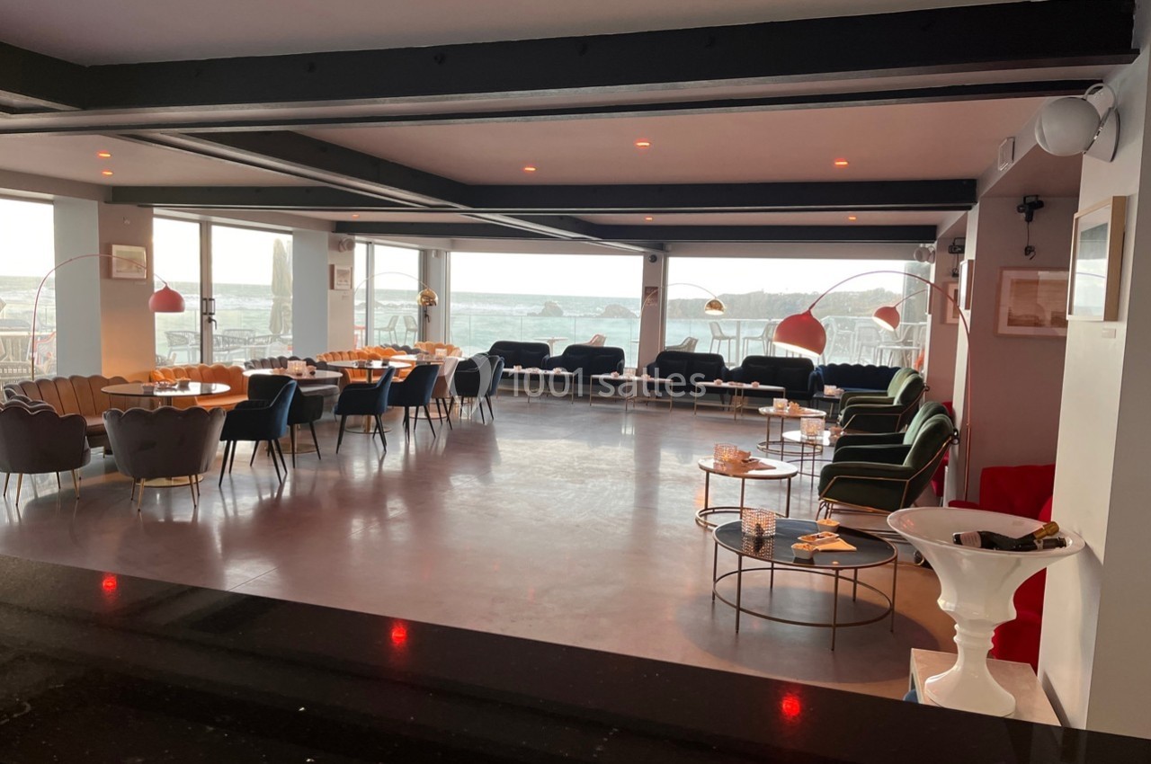 Salle lumineuse avec de grandes baies vitrées, mobilier moderne et vue sur un paysage extérieur.