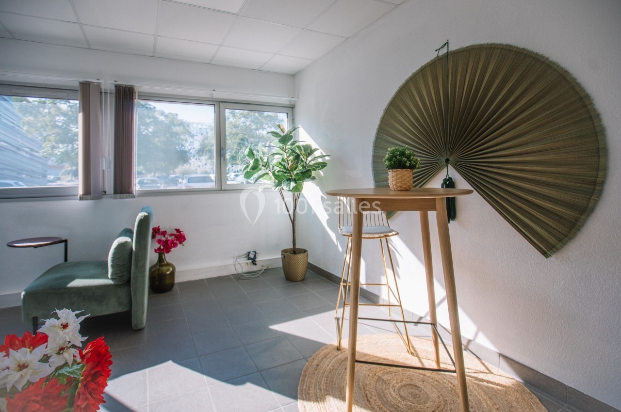 Espace lumineux avec table haute, chaise, plantes décoratives et éventail mural dans un intérieur moderne.