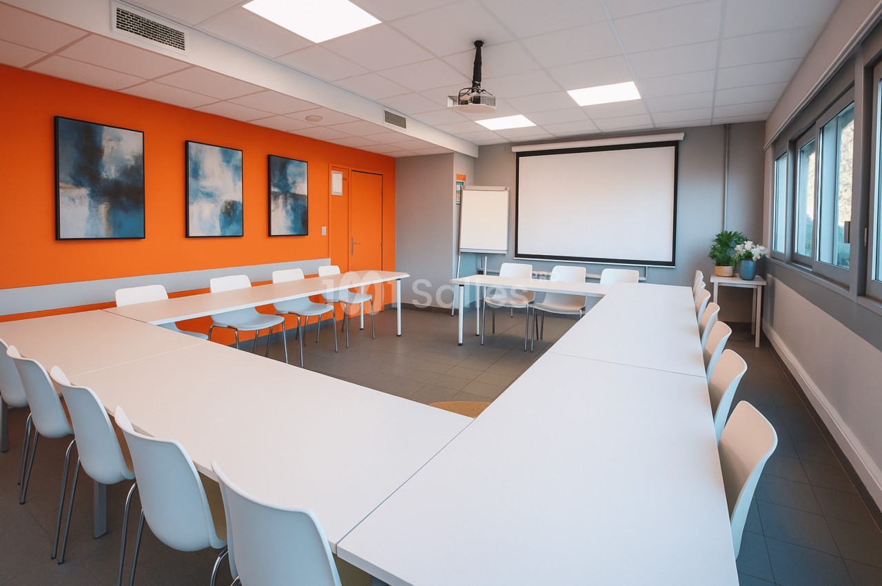 Salle de réunion en U avec tables blanches, chaises assorties, écran de projection et paperboard, murs orange et gris.