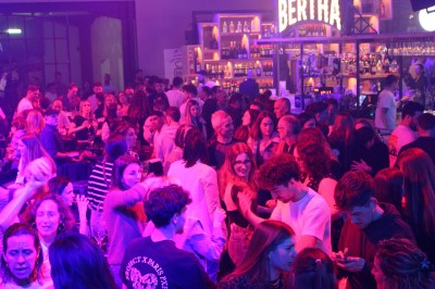 Personnes dansant et discutant lors d'une soirée en extérieur, éclairée par des lumières colorées et décorée de guirlandes.