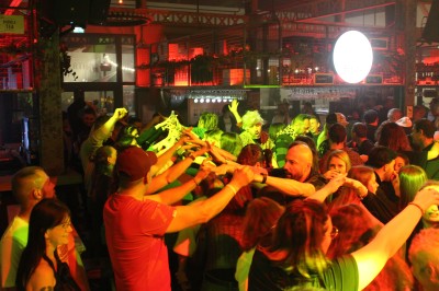 Personnes dansant et discutant lors d'une soirée en extérieur, éclairée par des lumières colorées et décorée de guirlandes.