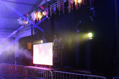 Personnes dansant et discutant lors d'une soirée en extérieur, éclairée par des lumières colorées et décorée de guirlandes.