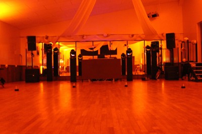 Personnes dansant et discutant lors d'une soirée en extérieur, éclairée par des lumières colorées et décorée de guirlandes.