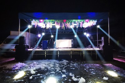 Personnes dansant et discutant lors d'une soirée en extérieur, éclairée par des lumières colorées et décorée de guirlandes.