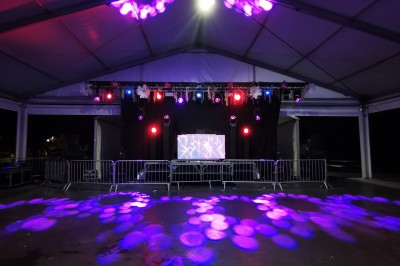 Personnes dansant et discutant lors d'une soirée en extérieur, éclairée par des lumières colorées et décorée de guirlandes.