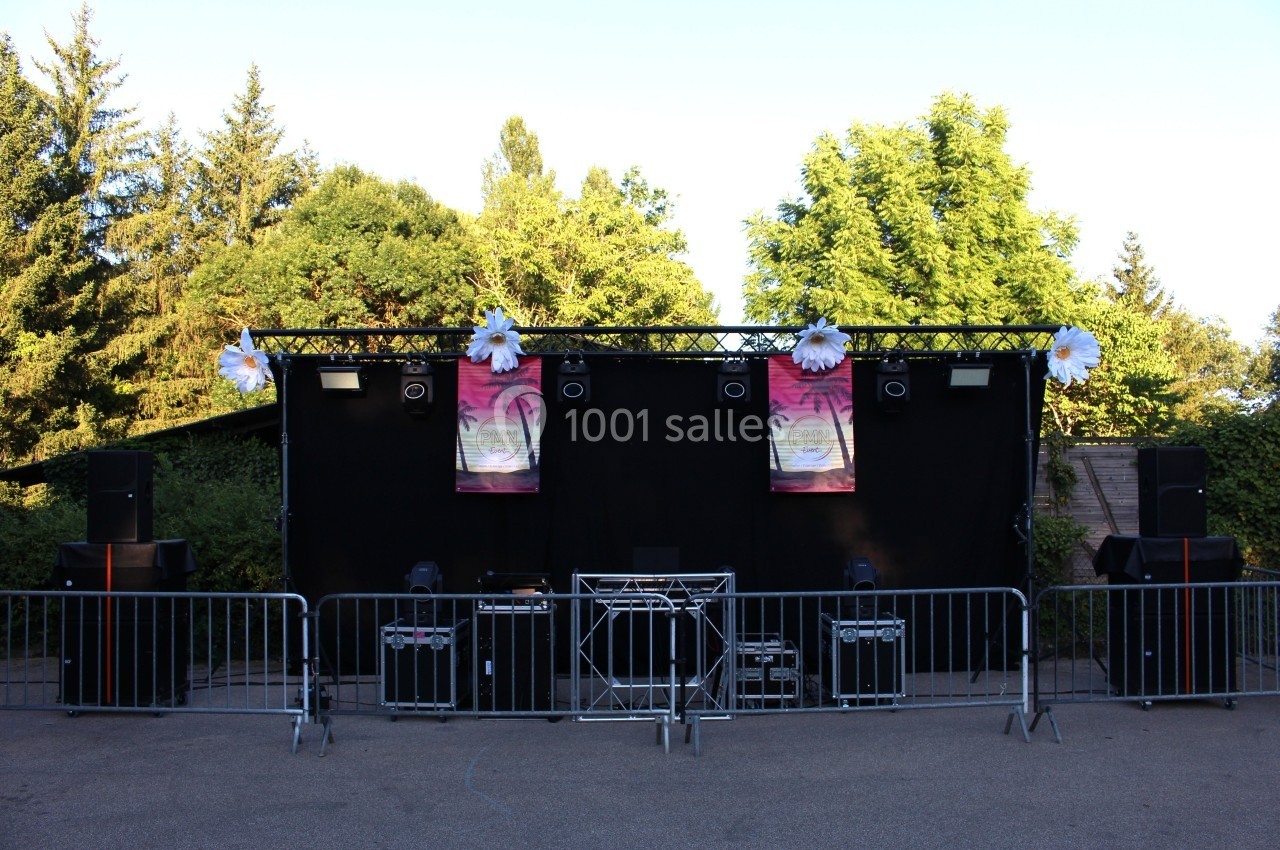 Scène extérieure avec éclairages, enceintes et décorations florales, entourée de barrières de sécurité.