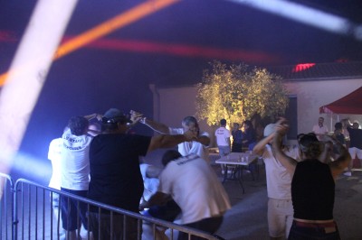 Personnes dansant et discutant lors d'une soirée en extérieur, éclairée par des lumières colorées et décorée de guirlandes.