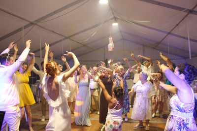 Personnes dansant et discutant lors d'une soirée en extérieur, éclairée par des lumières colorées et décorée de guirlandes.