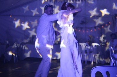 Personnes dansant et discutant lors d'une soirée en extérieur, éclairée par des lumières colorées et décorée de guirlandes.