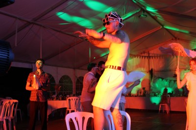 Personnes dansant et discutant lors d'une soirée en extérieur, éclairée par des lumières colorées et décorée de guirlandes.