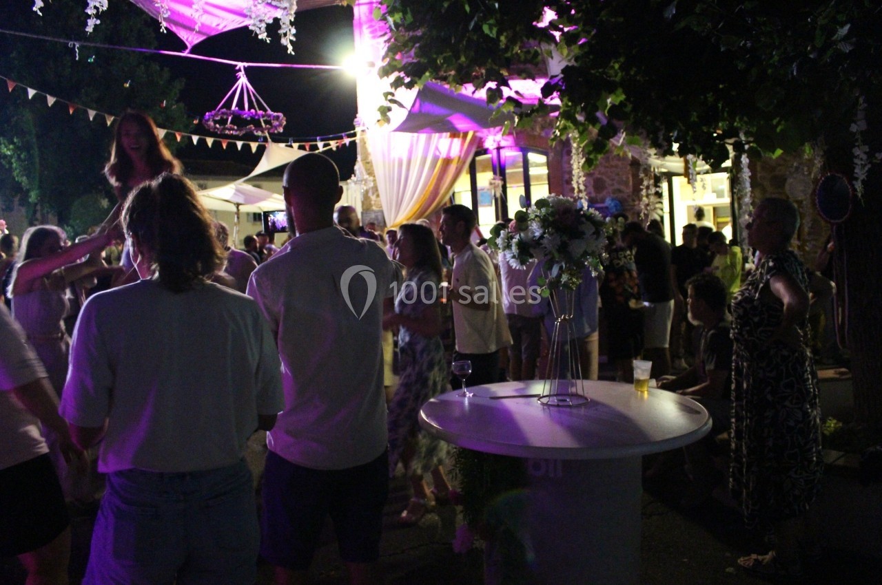 Personnes dansant et discutant lors d'une soirée en extérieur, éclairée par des lumières colorées et décorée de guirlandes.