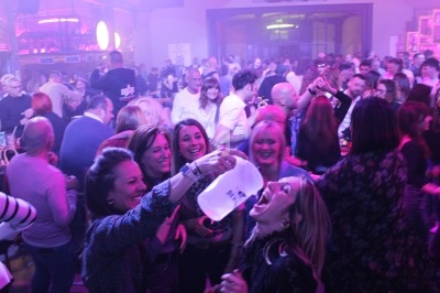 Groupe de personnes dans une ambiance festive et animée, éclairée par des lumières colorées dans un espace intérieur.