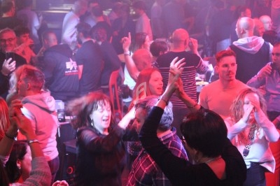 Personnes dansant et discutant dans une ambiance festive avec éclairage coloré dans un lieu bondé.