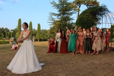 Une mariée lance son bouquet à un groupe de femmes souriantes dans un jardin par une journée ensoleillée.