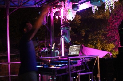 Un DJ mixant sur une scène éclairée par des lumières colorées, avec un ordinateur portable et des platines.