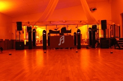 Salle de réception vide avec parquet, éclairage orange tamisé, équipements audio et décorations suspendues au plafond.